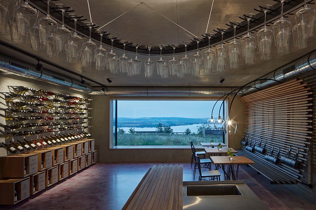 Nad barem je zavěšený velikánský lustr tvaru elipsy, která je součástí vizuální identity vinařství.