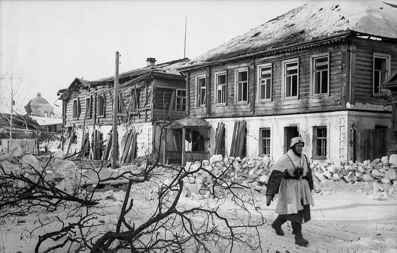 Německý voják před poničenými dřevěnými domy v Cholmu