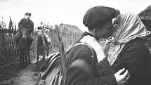 „Kolchoznice M. E. Nikolajeva se loučí se syny, kteří se přidávají k partyzánům. Líbá mladšího Ivana, starší syn Semen je už na koni.“ Fotografie Michaila Trachmanna ze série pořízené v roce 1942 ve vesnici Kruglovo v Pskovské oblasti