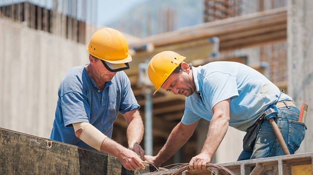 Stavební dělníci spolupracující při instalaci cementových bednění rámů.