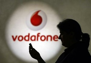 Žena s mobilním telefonem před logem mobilního operátora Vodafone. Ilustrační foto.