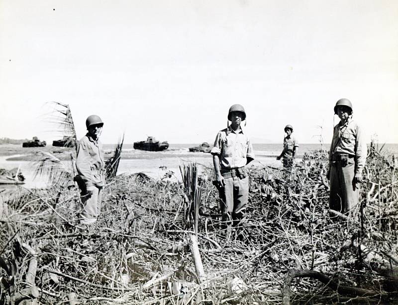 Příslušníci americké námořní pěchoty na zemi, která byla kdysi palmovým hájem. V pozadí japonské tanky zničené americkou střelbou