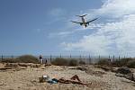 Žena se opaluje na pláži města Palma de Mallorca na španělských Baleárských ostrovech, nad pláží přelétá dopravní letoun chystající se k přistání (snímek z 29. července 2020)