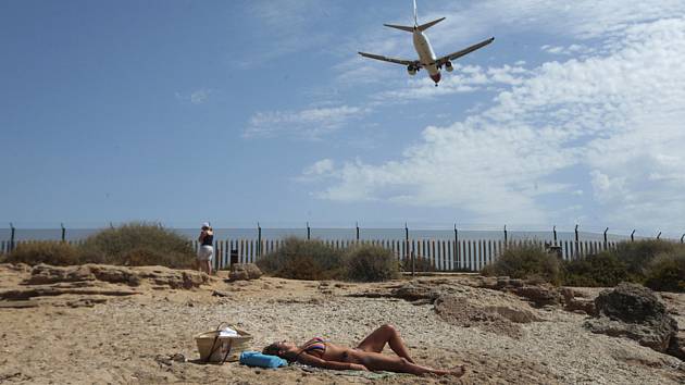 Žena se opaluje na pláži města Palma de Mallorca na španělských Baleárských ostrovech, nad pláží přelétá dopravní letoun chystající se k přistání (snímek z 29. července 2020)