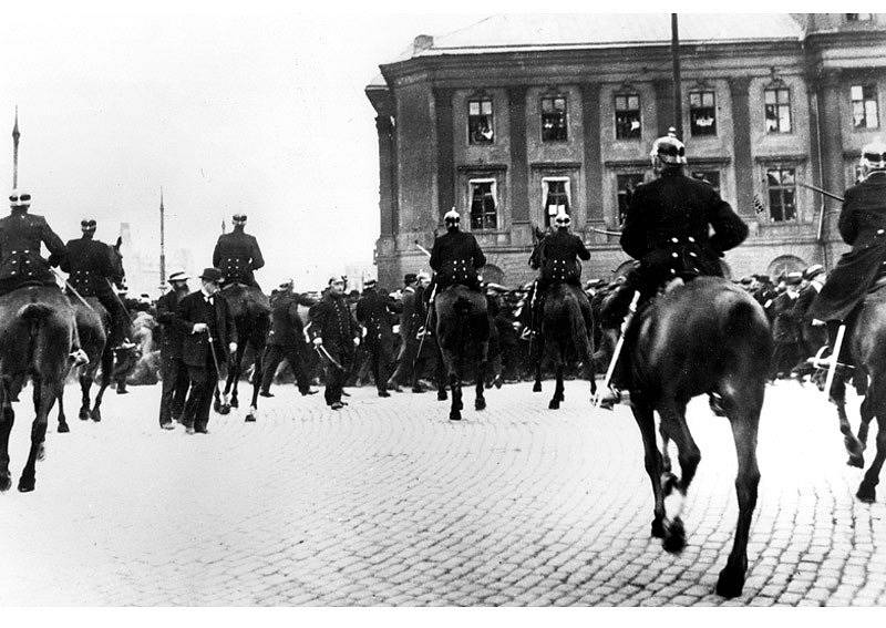 Policisté na koních rozhánějí v roce 1917 demonstraci ve Stockholmu na náměstí Gustava Adolfa. Postarší muž mezi policisty je Hjalmar Branting, vůdce švédských sociálních demokratů