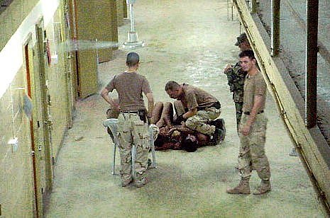 Abú Ghrajb, 25. října 2003. Desátník Graner se sklání, aby si promluvil se zadrženými, ležícími na podlaze vysvlečení donaha
