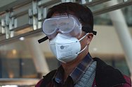 Muž v zamlžených brýlích a respirátorové masce čeká 15. dubna 2020 na nádraží v čínském Wu-chanu na vlak do Pekingu