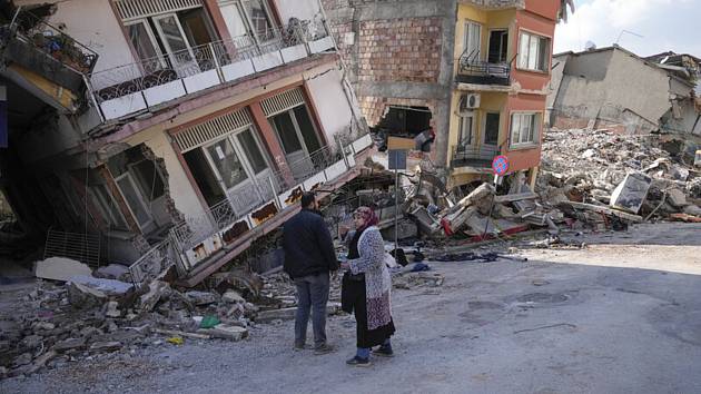 Lidé si povídají před troskami budov zřícené při zemětřesení v tureckém městě Hatay, 11. února 2023