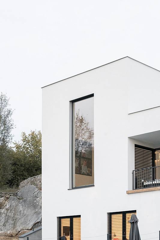 Kompaktní bílé hmotě vily dominuje vysoké okno do převýšeného obývacího prostoru