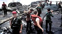 Zbylí vyčerpaní členové posádky Forrestalu stojí nad ohořelými troskami po palubním požáru, který si vyžádal životy 134 jejich druhů