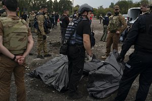 Ukrajinští vojáci a policisté stojí vedle zahalených těl lidí, kteří zemřeli po ruském útoku u Záporoží na jihu Ukrajiny 30. září 2022