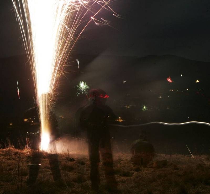  Mladí lidé oslavují příchod nového roku pomocí zábavné pyrotechniky na horizontu Bělského kopce na Šumavě, v pozadí masiv kopce Smrčina.