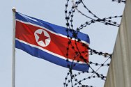 Severokorejská vlajka za ostnatým drátem. Ilustrační foto.