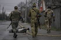 Ukrajinští vojáci po osvobození města Buča, před nimi mrtvý na silnici.