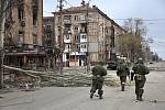 Proruští separatisté procházejí kolem poškozených obytných budov v ukrajinském Mariupolu, 16. dubna 2022.