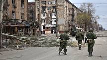 Proruští separatisté procházejí kolem poškozených obytných budov v ukrajinském Mariupolu, 16. dubna 2022.