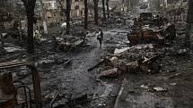 Žena kráčí ulicí města Buča lemovanou zničenými ruskými tanky.