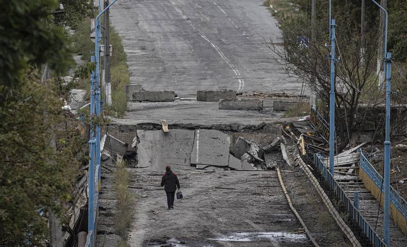 Žena kráčí po mostě, který se částečně zhroutil a poškodil v konfliktech mezi ruskými a ukrajinskými silami ve městě Balaklija v Charkovské oblasti