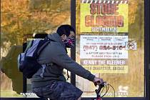 Muž s rouškou projíždí na kole kolem zavřeného obchodu ve městě Wilmette v americkém státě Illinois