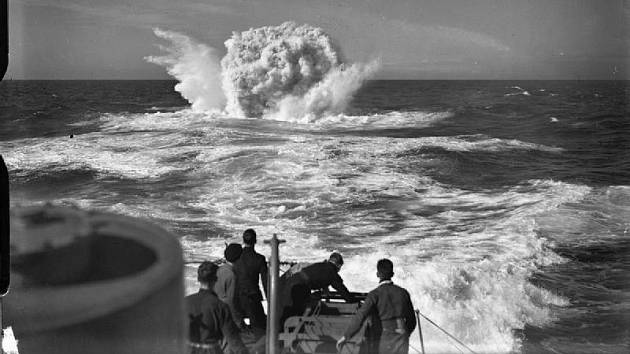 Několik mužů z posádky britského torpédoborce HMS Vanoc sleduje explozi hloubkových náloží, svržených v místě detekce ponorky.