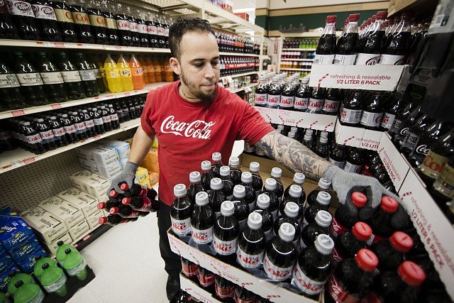 Pracovník obchodu skládá Coca-Colu do regálů.