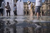 Lidé se v horkém letním počasí osvěžují ve fontáně v pařížském Louvre.