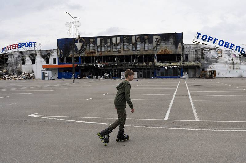 Chlapec bruslí na parkovišti před zničeným obchodním centrem, 30. května 2022, Buča, Ukrajina.