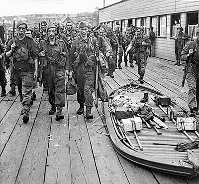 Commandos pochodují kolem složeného přepravního člunu, jenž se používal při menších výsadcích a sloužil k přepravě z motorových člunů na břeh