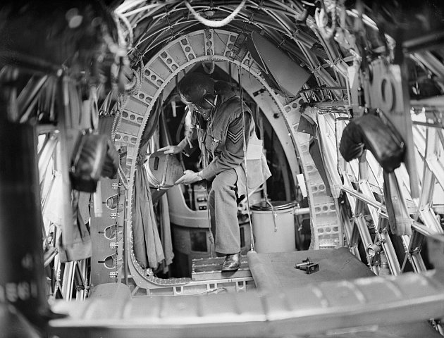 Člen posádky na palubě letounu Vickers Wellington umisťuje noční světlice na místo ve stísněné zadní části trupu. Vpravo lze vidět chemickou toaletu Elsan, kterou bylo velmi nepříjemné používat.