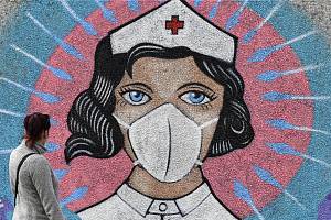 Žena se dívá 13. dubna 2020 v německém Hammu na graffiti pouličního umělce jménem Uzey. Malba zobrazuje zdravotní sestru s obličejovou maskou, na kterou útočí koronavirus v podobě šípů