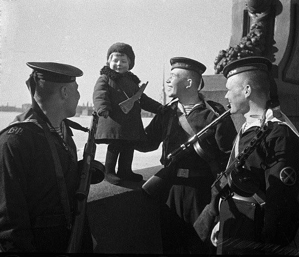 Námořníci Baltské flotily s malou holčičkou Ljusou, jejíž rodiče zemřeli během blokády. Leningrad, 1. května 1943
