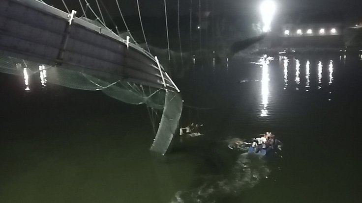 Nejméně 81 lidí zemřelo 30. října 2022 při zřícení visutého mostu pro pěší v indickém státě Gudžarát. Na snímku záchranáři prohledávají řeku v okolí zříceného mostu.