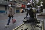 Žena v roušce prochází kolem bronzové sochy, která má na sobě také roušku, v čínském Wu-chanu (na snímku z 13. dubna 2020)