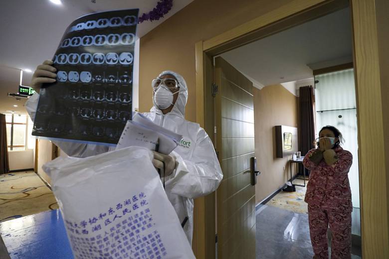 Lékař v ochranném oděvu si prohlíží rentgenový snímek během kontroly pacientů držených v karanténě kvůli koronaviru.