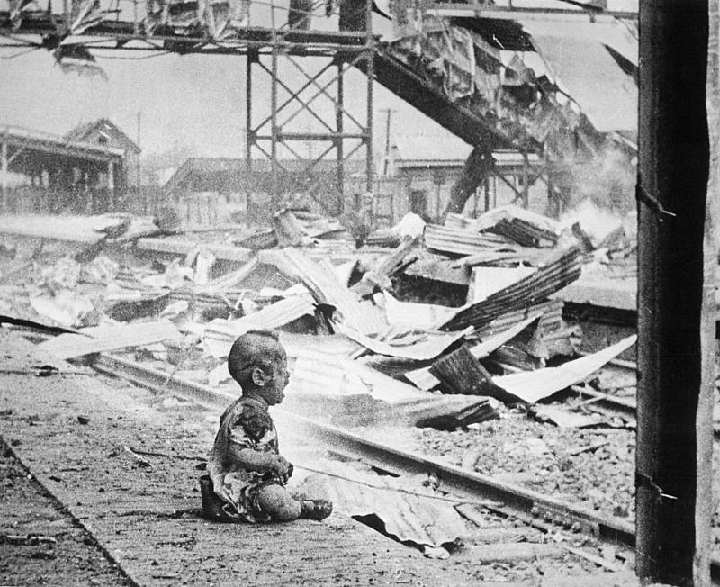 Krvavá sobota (Šanghaj, 1937). V ruinách rozbombradovaného nádraží plačící zraněné batole, jehož matka leží poblíž mrtvá. Druhá čínsko-japonská válka. Ikonický obrázek čínského fotožurnalisty H. S. „Newsreel“ Wonga 