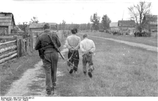 Voják Waffen-SS před sebou žene dva spoutané muže označované za sovětské partyzány