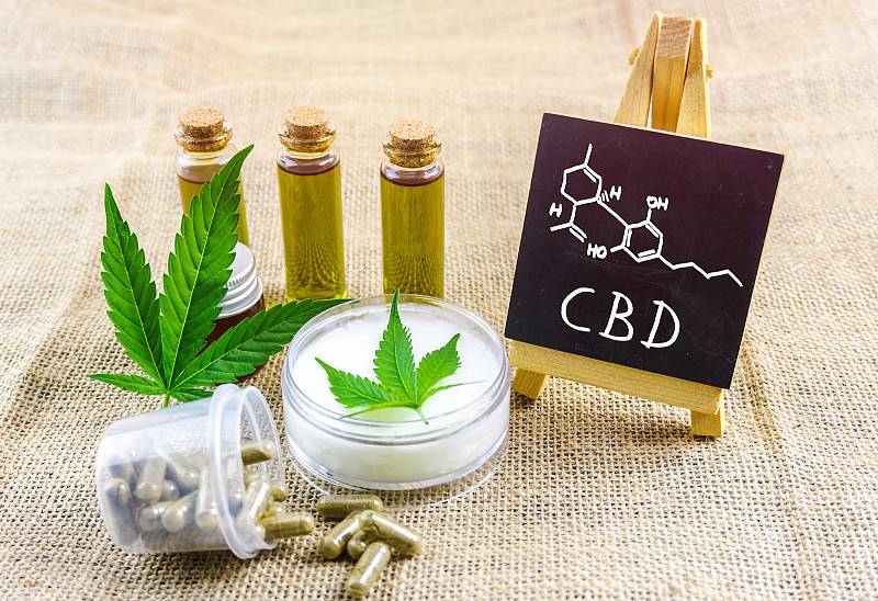 CBD a THC konopné oleje, pilulky a cbd krém s chemickou strukturou na tabuli.