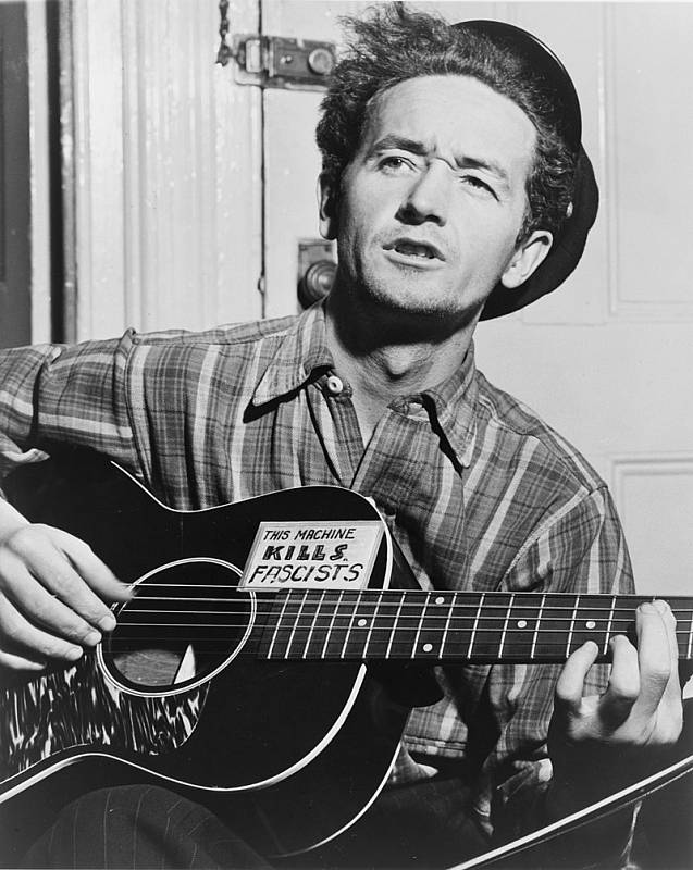 Americký písničkář Woody Guthrie s kytarou vyzdobenou nápisem: "Tento nástroj zabíjí fašisty." Zničení lodi Reuben James věnoval Guthrie jednu ze svých nejslavnějších písní