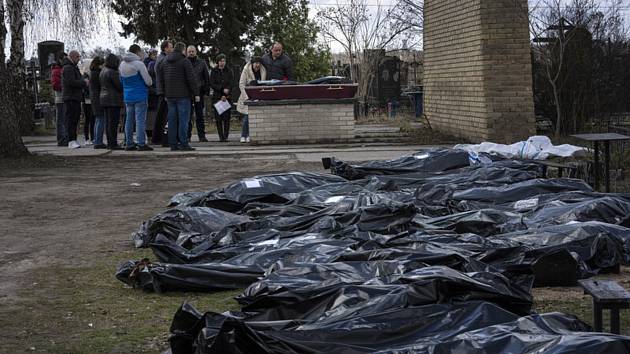 Těla exhumovaná z masového hrobu v ukrajinském městě Buča. V pozadí se rodina loučí z jednou z obětí ruské invaze, 11. dubna 2022