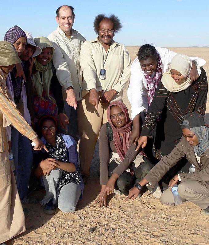 Doktor Muawia Shaddad a Peter Jenniskens z NASA ukazují spolu s několika studenty univerzity v Chartúmu na jeden z úlomků asteroidu 2008 TC3