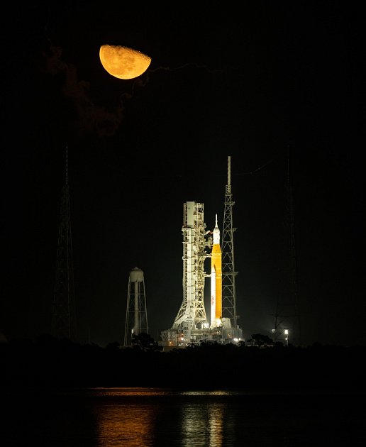Měsíc nad raketou NASA Space Launch System (SLS) s kosmickou lodí Orion na palubě odpalovací rampy.