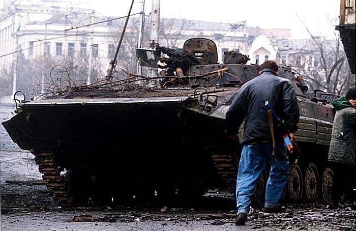 Čečenský ozbrojenec běží kolem spáleného ruského obrněného vozidla (BMP-2) během bitvy o Groznyj