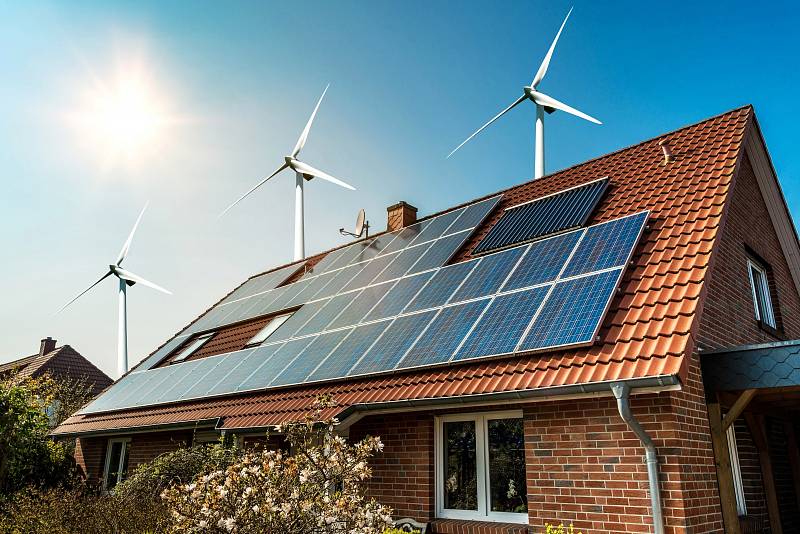 Solární panely na střeše domu a větrné turbíny - koncept udržitelných zdrojů.