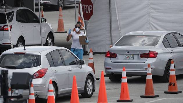 Zdravotnice v roušce se pohybuje mezi auty, která stojí ve frontě v americkém Miami Gardens. Řidiči čekají na testování na covid-19.