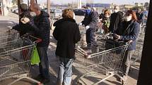 Lidé s rouškami čekají před obchodem v Casalpusterlengu na severu Itálie