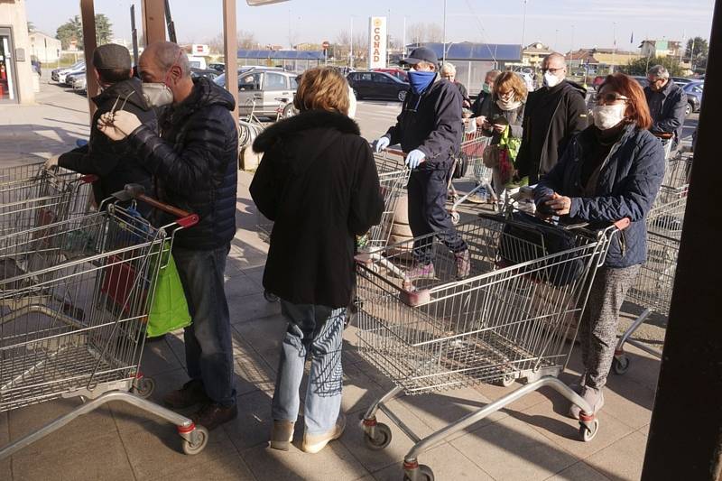 Lidé s rouškami čekají před obchodem v Casalpusterlengu na severu Itálie