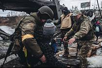 Ukrajinští vojáci ve městě Irpiň pomáhají civilistům překonat řeku. Most v pozadí Ukrajinci zničili, aby zpomalili postup ruských vojsk.