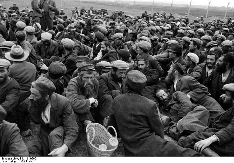 Krakovská oblast, konec roku 1939. Zajatí Židé, sehnaní na otrocké práce, sedí na otevřeném prostranství obklopeném novým plotem z ostnatého drátu