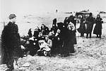 Židovské ženy a děti hlídané krátce před svým zavražděním příslušníky lotyšské policie v roce 1941. K masakrům docházelo na více místech, tento snímek zachycuje událost v lotyšském přístavu Liepaja