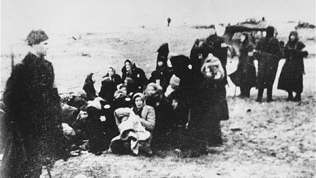Židovské ženy a děti hlídané krátce před svým zavražděním příslušníky lotyšské policie v roce 1941. K masakrům docházelo na více místech, tento snímek zachycuje událost v lotyšském přístavu Liepaja